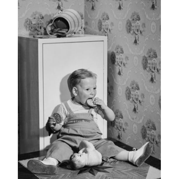 Baby boy leaning against a cabinet and eating cookies ...