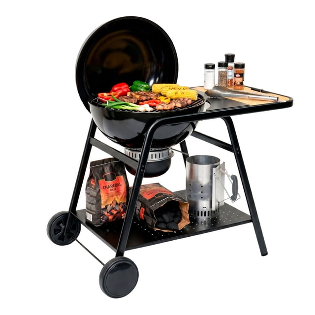 asador de carbón 22 pulgadas, 58 cm con mesa lateral auxiliar y ruedas transportadoras avera ac55mml Barbacoa de carbón negra, vista frontal 3/4 con tapa abierta; parrilla redonda de 58 cm y doble rejilla con verduras y cortes, mesa lateral para condimentos y pinzas, termómetro en la tapa y ventililla superior visibles, cuerpo de acero esmaltado, bandeja de ceniza y bandeja inferior con bolsas de carbón, estructura total de 117 cm sobre patas con ruedas para traslado; también es adecuada para ahumar pequeñas porciones regulando la ventilación.
