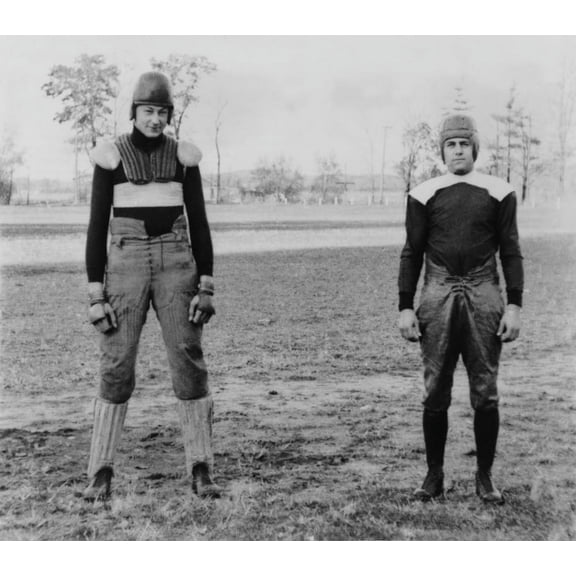 Notre Dame University Football Players Wearing Old And New Football Uniforms. At Left Is A Football Suit Of The 1880'S With External Padding. At Right Is A 'Modern' Uniform With Shoulder Pads Worn