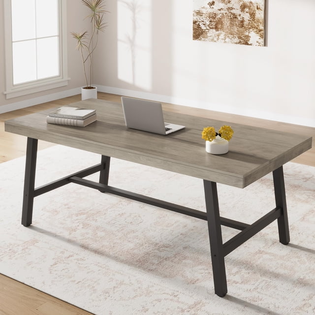 GloryStar Industrial Computer Desk, 70.87-inch long large executive PC study home office desk in grey. This modern wood desk features a spacious MDF wood tabletop with a dust-proof and waterproof surface, supported by sturdy 2x2-inch metal legs and a T-shaped steel bar structure for excellent stability. The desk includes adjustable non-slip foot pads to protect floors and ensure balance on uneven surfaces. Its ergonomic design offers a 30-inch height for comfortable legroom, making it ideal for work or study. Shown in a bright home office setting with a laptop, books, and a small vase on the desk.