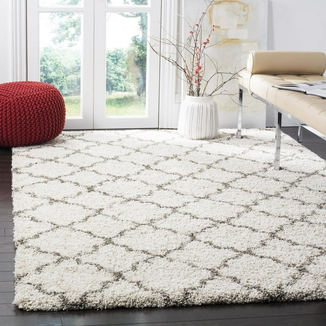 Safavieh Hudson Jaye white shag area rug featuring a gray geometric lattice design, styled in a bright living room with dark wood floors, beige bench seating, and decorative vase.