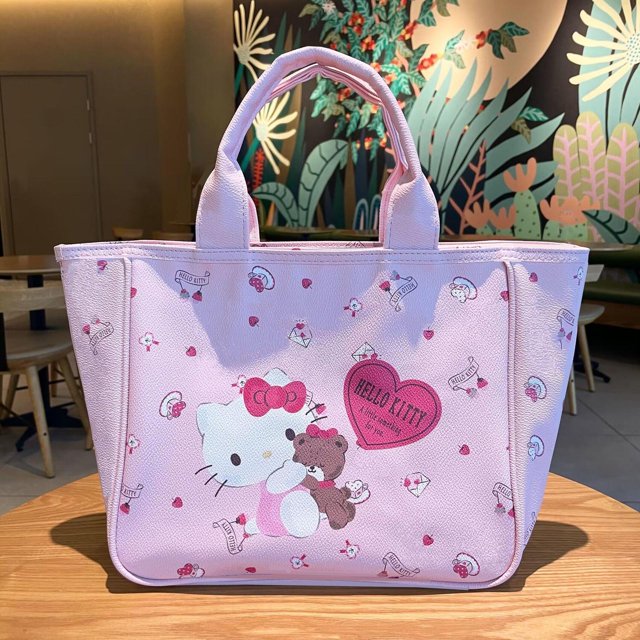mochila de un solo hombro con estampado de leopardo rosa de hello kitty de pu de hello kitty con forma de corazón para chica amorosa, de gran capacidad, color Gato kt de amor rosa; vista frontal centrada de mochila rectangular rosa con asas superiores, panel frontal con Hello Kitty abrazando un osito y un corazón rosa que dice 'Hello Kitty', superficie de PU granulada y pequeños motivos repetidos, colocada sobre mesa de madera en un interior.