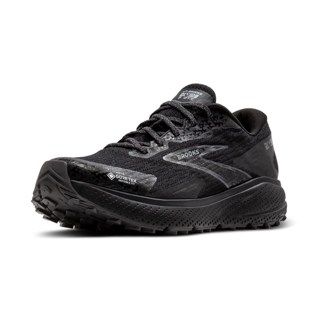 zapatilla impermeable para trail running brooks divide 5 gtx para mujer Zapatilla negra Brooks Divide 5 GTX para mujer, vista 3/4 frontal; malla y paneles sintéticos negros con logo Brooks y etiqueta GORE-TEX visible, cordones planos y lengüeta tipo fuelle, entresuela DNA LOFT v2 elevada en negro y suela TrailTack con tacos agresivos para tracción en senderos; adecuada también para trotes urbanos y transiciones a rutas de trail ligero.