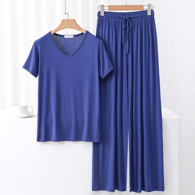TACILIP Ensembles 2 Pcs pour Femmes Ensembles de Détente d'Été Comprenant un Haut à Manches Courtes à Col en V Bleu Uni et un Pantalon à Jambes Larges Assorti. Fabriqué à Partir d'Un Mélange Doux et Respirant de modal, Coton et polyester, Cet Ensemble de Pyjama Est Conçu pour le Confort et la Détente. Idéal pour Se Détendre, Dormir Ou Porter à l'Intérieur de Façon Décontractée. l'Ensemble Est Exposé sur des Cintres en Bois sur un Fond Blanc Minimaliste.
