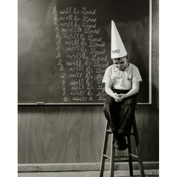 Boy wearing a dunce cap sitting in front of a blackboard Poster Print