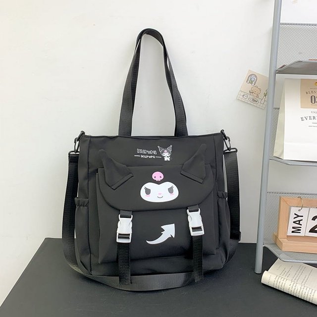 bolso de hombro minimalista, bolso pequeño de estilo juvenil, bolso de tutoría de moda para estudiantes universitarios, bolso de tela oxford, bolso de mujer negro Heldig. Vista frontal centrada de bolso cuadrado de tela Oxford negra con asas de mano y correa ajustable; solapa con hebillas blancas y cierre, bolsillo exterior con estampado de personaje blanco y rosa, costuras visibles y bolsillos laterales abiertos; compacto y apto para escuela y uso diario.