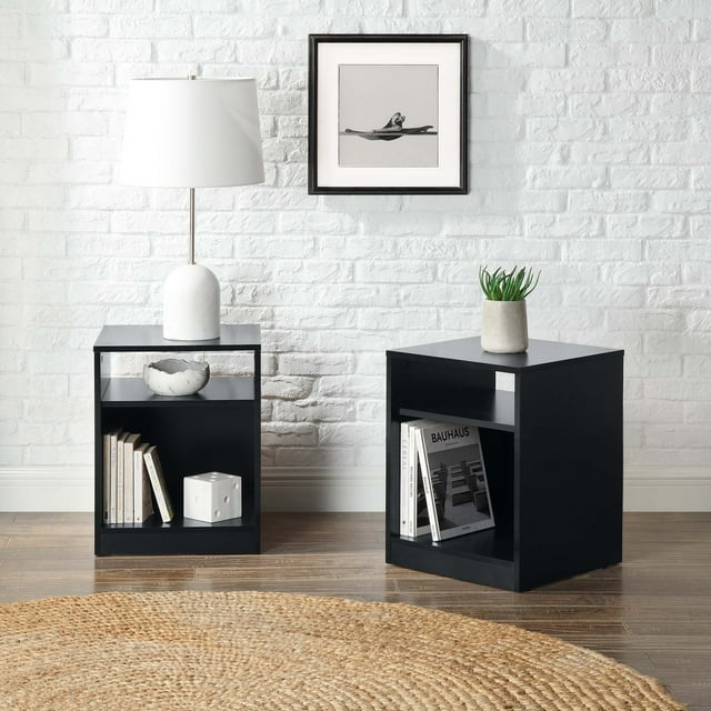 Set of two black Mainstays open shelf nightstands styled with books, a white table lamp, and small decor pieces against a white brick wall.
