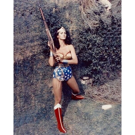 Lynda Carter as TV's Wonder Woman holding up rifle standing by wall 8x10 photo