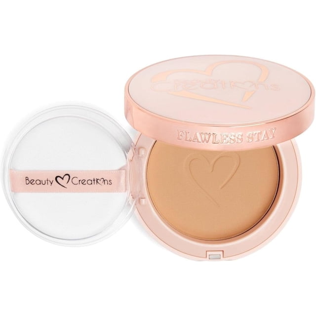 beauty creations flawless stay – polvo compacto (fsp6.5) cobertura media a completa acabado aterciopelado libre de aceites y cruelty-free, compacto rosa metalizado abierto con polvo fijador beige y relieve de corazón, incluye aplicador-esponja blanca con cinta rosa y logo, vista frontal sobre fondo blanco.