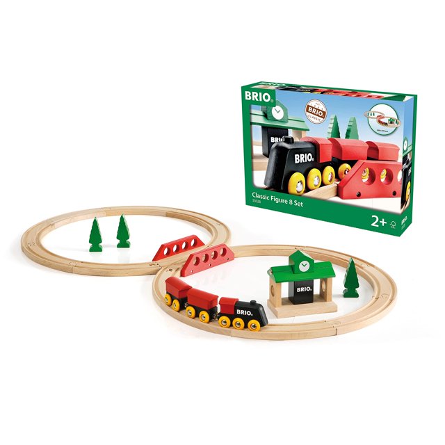 toy train set brio world classic, figura 8, 22 piezas, 2 años o más Vista cenital del set de tren de madera en forma de 8 con 14 rieles ensamblados, locomotora motorizada negra con dos vagones rojos, puente de cruce rojo, estación verde con logo BRIO y tres árboles verdes sobre fondo blanco; a menudo usado también para introducir conceptos de rutas y coordinación en juego imaginativo.