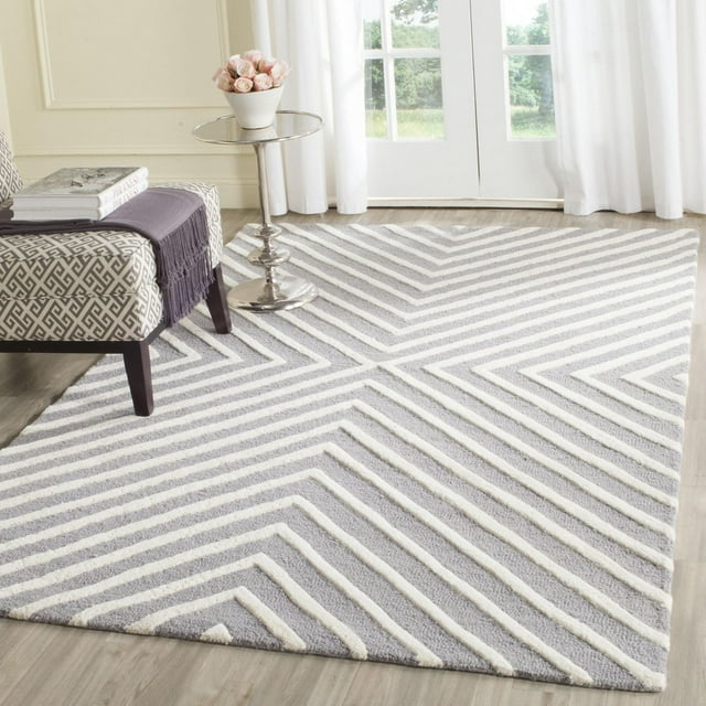 Safavieh Cambridge Lilly Diamond Stripes area rug in gray and white, displayed on light wood floor near patterned bench and small round table with flowers.