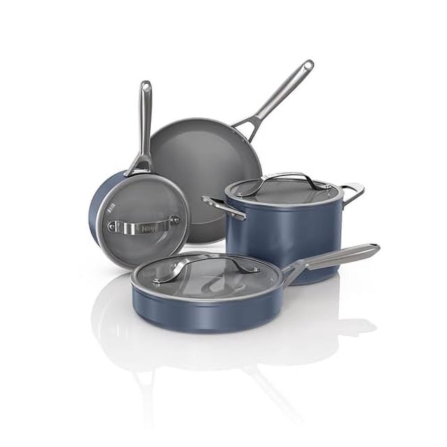 ninja neverstick ceramic pro juego de utensilios de cocina de 7 piezas, set azul medianoche con dos sartenes, una sartén baja, una cacerola y una olla profunda, todas con tapas de vidrio; interiores grises de revestimiento cerámico NeverStick y mangos de acero inoxidable, vista en 3/4 sobre fondo blanco, apto para estufa y horno y a menudo usado para cocinar por lotes o asar a la parrilla en horno.