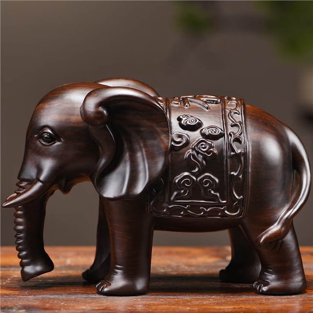 ebony solid wood carved elephant figurines, a pair of auspicious ornaments for home living rooms, used to fill in missing corners and decorate. Figura única hembra de ébano, 28 cm, vista 3/4 sobre superficie de madera; talla manual en madera maciza con vetas oscuras pulidas, manta tallada decorativa en el lomo, trompa curvada y orejas detalladas; ideal como adorno de sala y regalo empresarial.