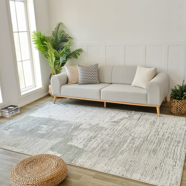 Rug Branch Nomad Abstract indoor area rug in green and beige tones placed in a modern living room setting beneath a light gray sofa with chevron and textured pillows.