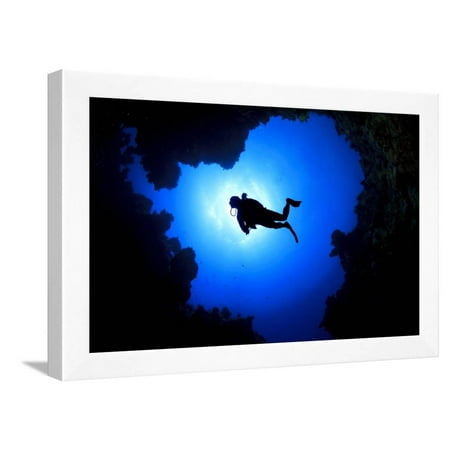 scuba diver swims over underwater cave silhouette against sun