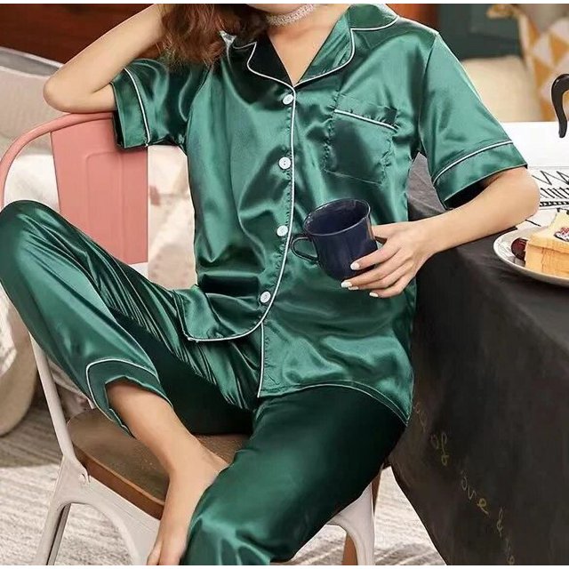 pijama de satén personalizado para pareja, conjunto de ropa de dormir corta y larga ideal para regalo de aniversario boda novia y novio — mujer sentada con pijama satén verde liso; camisa de manga completa con cuello liso, botones frontales y bolsillo en el pecho, pantalón hasta el tobillo de corte recto y tela brillante con caída suave; a menudo usado por parejas para sesiones de fotos de aniversario o como conjunto de descanso coordinado.