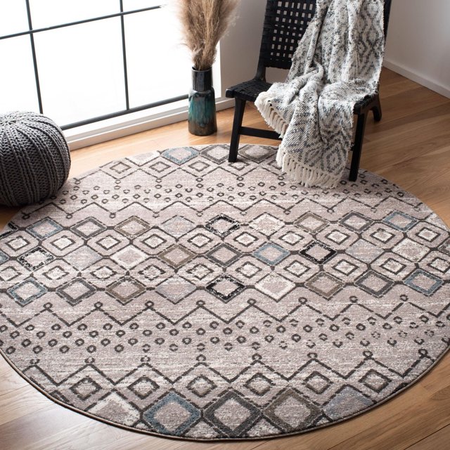 Round SAFAVIEH Amsterdam Gladwin geometric area rug in beige, gray, and blue tones on wood floor beside black chair with fringed throw.