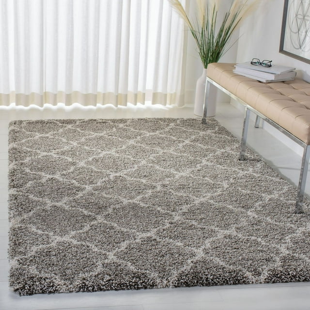 Safavieh Hudson Jaye gray and white geometric shag area rug displayed in a bright room with light flooring, beige bench, and tall vase with pampas grass.