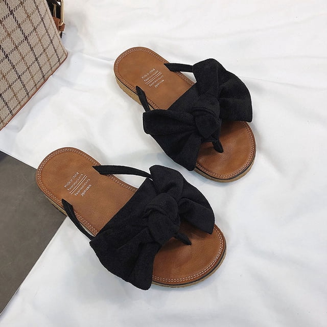chanclas diarias de verano ocio playa arco zapatillas planas para mujer wmkox8yii ytu5339 negro. Vista cenital de sandalias planas negras para mujer con plantilla marrón, tiras tipo dedo y gran lazo anudado en la parte superior, suela plana de 2 cm con costura visible, sobre fondo de tela blanca; también adecuadas como sandalia ligera para paseos y ocio.