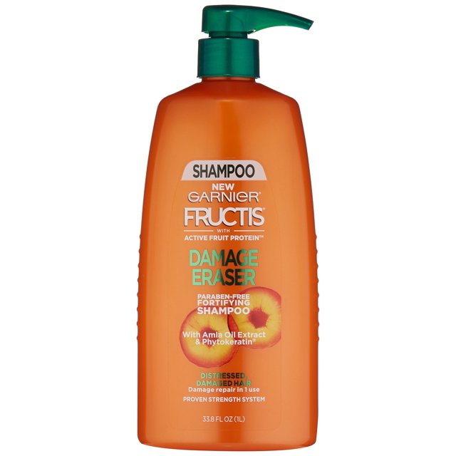 champú garnier fructis damage eraser para cabello desgastado y dañado Botella frontal naranja de 33.8 oz (1L) con dispensador verde; etiqueta con logo Garnier Fructis, texto "Damage Eraser", gráfico de amla y menciones de proteína activa y extracto de aceite de amla, formulado para reparación intensiva del cabello desgastado y dañado en rutina de cuidado capilar.