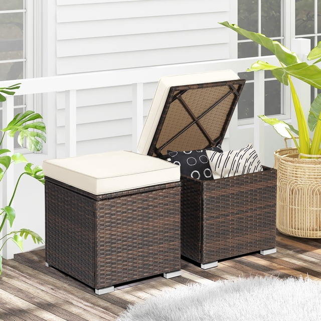 Gymax 2PCS Outdoor Patio Ottomans Hand-Woven PE Wicker Footstools with removable off-white cushions. The ottomans feature a mix brown hand-woven PE wicker design with hidden storage space accessible via hinged tops. Each ottoman measures 16'' x 16'' x 15.5'' and includes a soft, padded cushion for comfort. Suitable for outdoor use with a sturdy steel frame and raised feet for durability. Shown on a patio with one ottoman open, revealing storage with decorative pillows inside.
