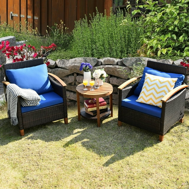 Gymax Ensemble de Conversation en Rotin Osier pour Patio 3 Pcs Ensemble de Meubles d'Extérieur avec Coussin. Cet Ensemble Comprend Deux Chaises en Osier avec Coussins Bleus et Accoudoirs Ergonomiques, et une table Basse Ronde à Deux Niveaux avec un Dessus en Bois d'Acacia et une Tablette en Osier Inférieure. les Chaises Sont Faites de Rotin et de Bois d'Acacia Résistants aux Intempéries, Supporte jusqu'à 360 Lb Chacune. la table Basse Offre de l'Espace pour les Boissons et la Déco. Présentée dans un Jardin avec une Verdure Luxuriante et des Fleurs.