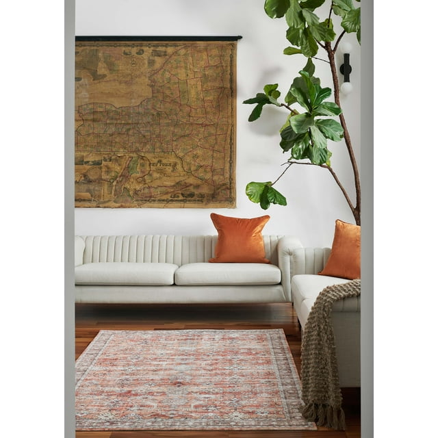 Ruby traditional area rug with detailed floral and geometric patterns on hardwood floor between beige sofas accented by orange pillows and a large green plant.