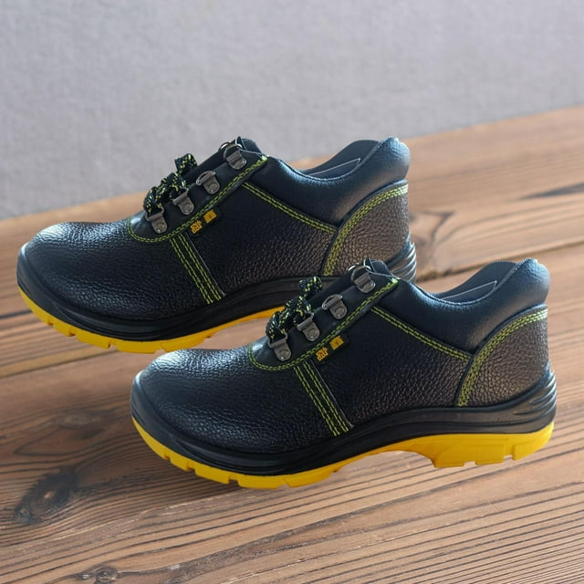 zapatos de trabajo de seguridad shamjiam para hombre con punta de acero resistente us 9.5 negro, vista 3/4 lateral de par de botas bajas de cuero PU con costuras verdes y ojales metálicos, cordones bicolor, suela amarilla de poliuretano de alta densidad antideslizante; entresuela con placa de acero según especificación y plantilla transpirable visible; colocadas sobre piso de madera. Suelen usarse para trabajo industrial y de construcción.