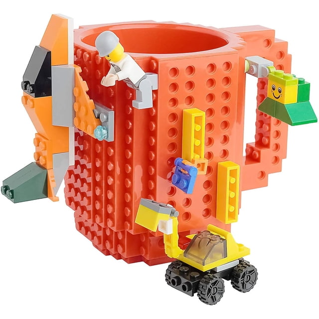 taza de bloques Roja AJR, vista 3/4 frontal; taza plástica tipo ladrillo de 15cm x 15cm y 355ml con superficie para montar bloques, incluye paquete de bloques y un muñequito o vehículo al azar montados; caja transparente con nombre “Build-on Brick Mug” visible. Puede usarse con líquidos muy calientes; se recomienda lavar a mano. A menudo se usa también para organizar piezas pequeñas de construcción.