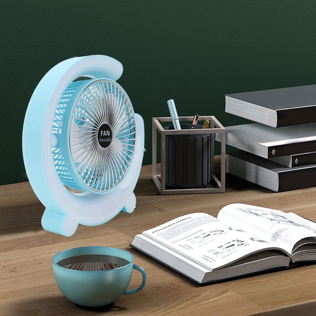 ventilador de mesa portátil de 5 pulgadas anggrek recargable por usb, ABS azul claro con rejilla circular y aspas visibles, base de cuatro patas estable, inclinación 180 grados, batería interna 1800 mAh y puerto USB; sobre escritorio junto a libros y taza, a menudo se usa para ventilación personal en dormitorio u oficina.