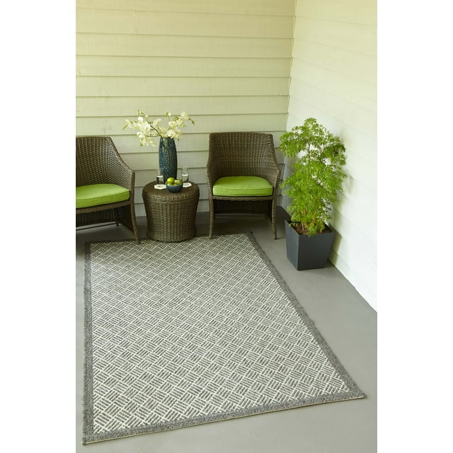 ECARPET Eve contemporary area rug featuring a gray and white geometric design, displayed on an outdoor porch setting with two brown wicker chairs, green cushions, small round table holding decorative items, and potted plant.