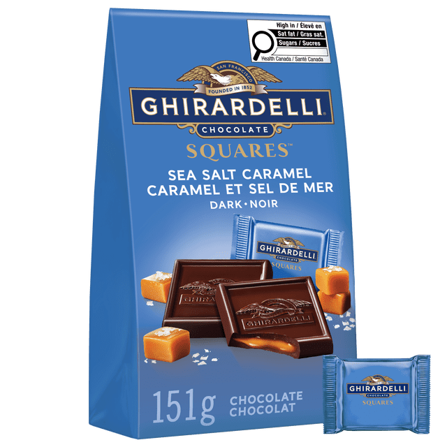 GHIRARDELLI Sea Salt and Caramel Dark Chocolate Squares, 151-gram bag with blue packaging featuring the Ghirardelli logo and gold eagle emblem. The front shows two dark chocolate squares embossed with the brand name, one broken to reveal flowing caramel inside, surrounded by caramel cubes and sea salt flakes. Individually wrapped squares in blue foil are visible, combining rich dark chocolate with salted caramel, suitable for sharing or gifting.