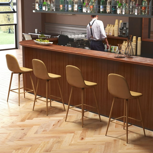 Homy Casa set of 4 swivel 26 inch bar stools with brown PU upholstered seats and footrests, ergonomic curved backs, and matte black metal legs, arranged at a wooden kitchen or home bar counter with a bartender in the background, suitable for kitchen islands or dining areas.