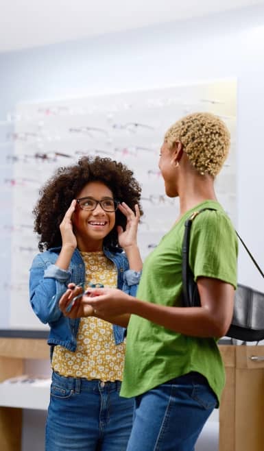 Child trying on eyeglasses with an adult nearby.