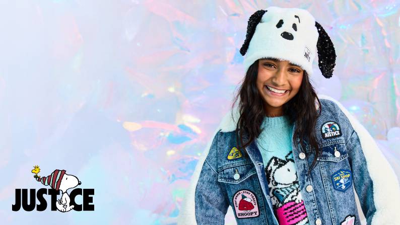Girl wearing Snoopy ear hat, denim jacket with playful patches, and blue sweater with Snoopy graphic.