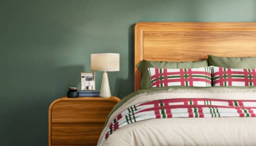 A festive bedroom is decorated with green walls, wooden furniture, and plaid holiday bedding in red, green, and cream tones.