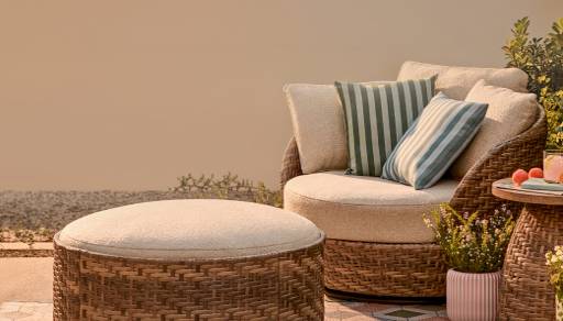 Beautiful by Drew patio furniture. Wicker armchair with upholstered cushions and ottoman. Decorative pillows, outdoor rug and side table.