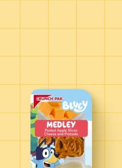 A Bluey Crunch Pak with peeled apple slices, cheese, and pretzels against a yellow tile background.