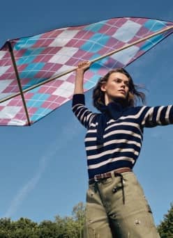 Woman in a blue-and-white striped knit sweater with olive pants and brown belt, holding a kite.