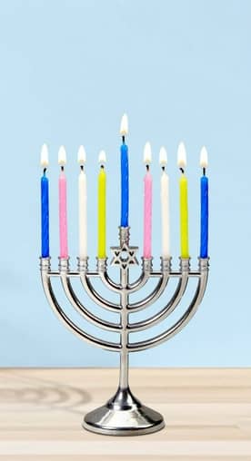 Image shows a lit menorah with colorful candles on a table with a blue background.