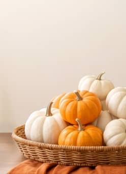 A shallow basket full of mini orange and white pumpkins on a table with an orange tablecloth.