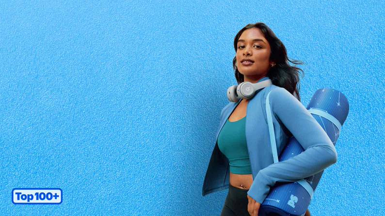 A model wears blue activewear, grey headphones and carries a yoga mat. A badge reads: top one-hundred plus.