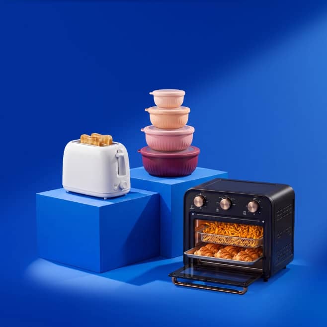 White toaster with toast, black countertop oven with fries and croissants, and stacked pink food storage containers on blocks.