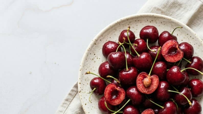 A plate of fresh cherries, some sliced, on a counter.