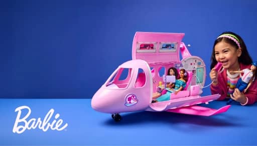 Barbie airplane playset with dolls open to show interior while a child smiles and holds a Barbie doll.
