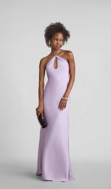 A woman is wearing a lavender dress with a keyhole neckline carrying a black clutch.