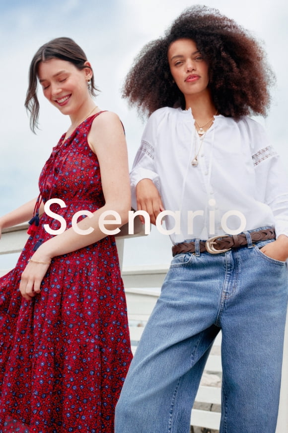 Two women: one in a red floral sleeveless dress with tasseled ties, one in a white blouse with tasseled ties, wide leg jeans and layered necklaces.