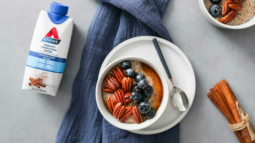 Bowls of fruit and granola on a grey table with Atkins protein shakes and sticks of cinnamon nearby