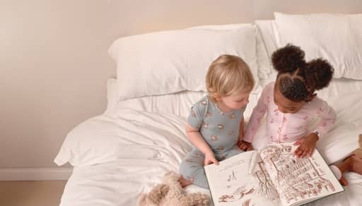 Two toddlers are shown reading a book in bed