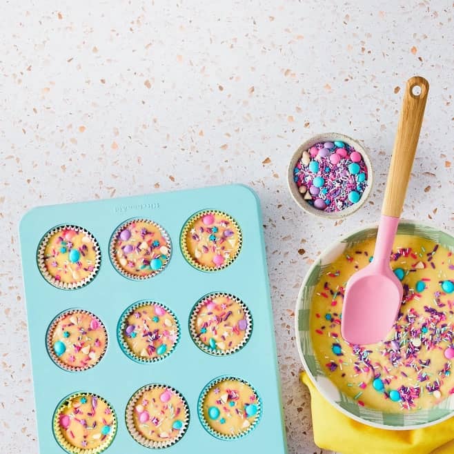 A blue muffin tray is shown with yellow sprinkle batter in the cups and then a side of sprinkles.